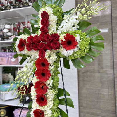 Standing cross-shaped arrangement of red roses and gerberas with white and green blooms on a metal easel.