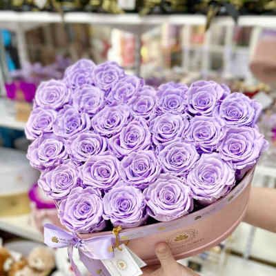 Heart-shaped box filled with tightly packed lavender roses held in both hands