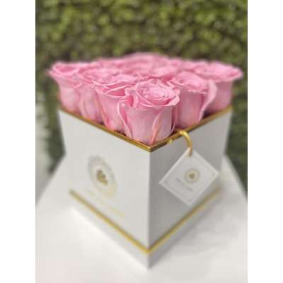 Square white box filled with tightly packed pink roses on a white surface