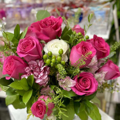 Bright pink rose arrangement with white accent blooms and green berries in a clear glass cube vase