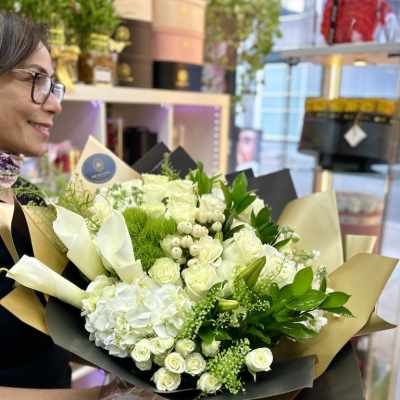 Large hand-tied bouquet of white roses, hydrangeas, and calla lilies wrapped in black and gold paper