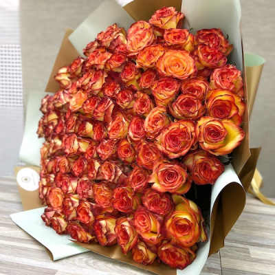 Large wrapped bouquet of tightly clustered orange and red roses on a wooden surface