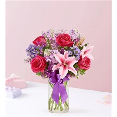 Pink roses and lilies in a clear glass vase with a purple ribbon