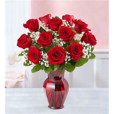 Red roses arranged in a red glass vase with white filler flowers