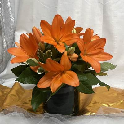 Orange lilies arranged in a black vase with dark green foliage