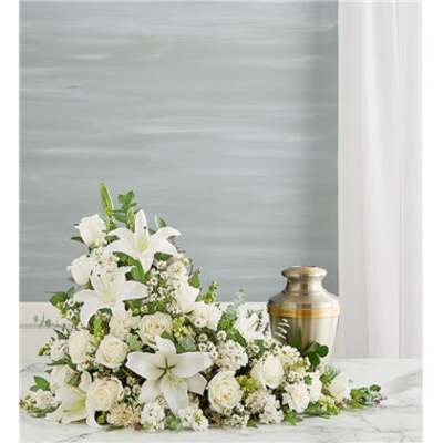 White floral funeral spray with lilies and roses beside a brass urn