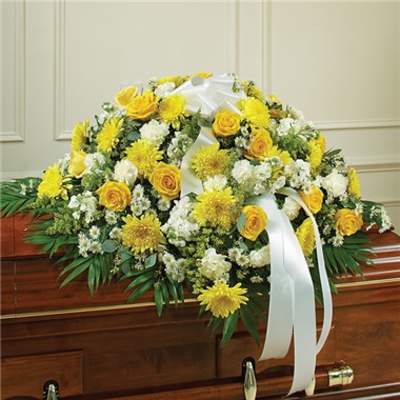 Yellow and white funeral spray on a casket with white ribbon