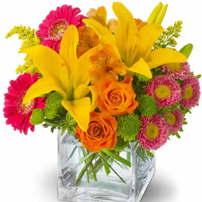 Bright mixed bouquet in a clear square glass vase with yellow lilies and pink daisies