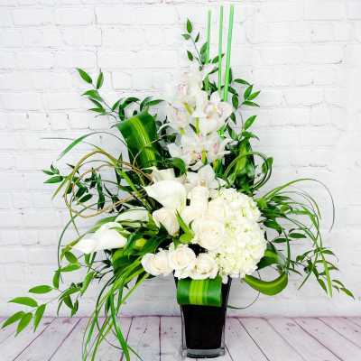 Tall white floral arrangement in a black vase with orchids, calla lilies, and roses