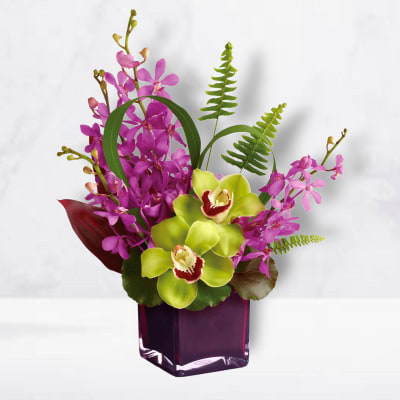 Purple orchids and green cymbidium orchids in a purple glass vase