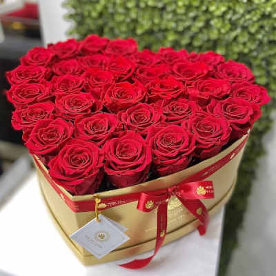 Heart-shaped gold box filled with red roses and tied with a red ribbon and tag