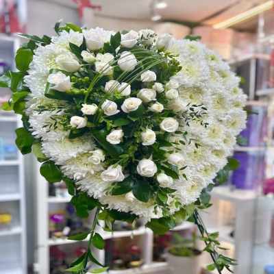 Heart-shaped white floral sympathy wreath with white roses and trailing greenery