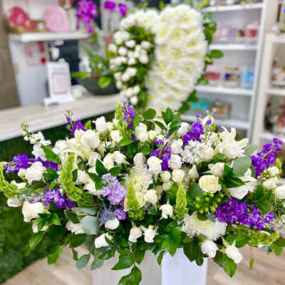 Large white and purple floral arrangement on a tall white pedestal in a flower shop