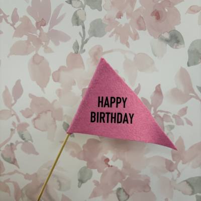 Pink felt birthday pennant on a wooden stick against a floral background