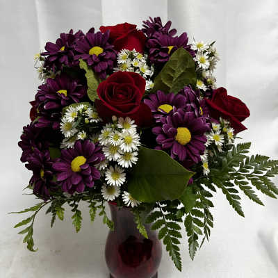 Bouquet of red roses and purple daisies in a burgundy vase