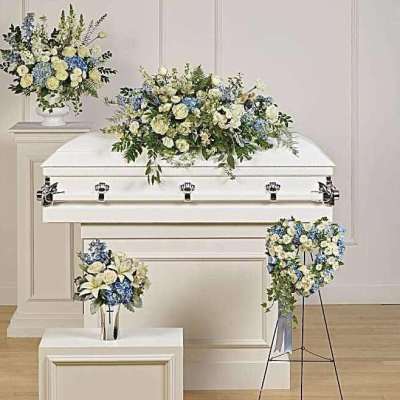 White casket with blue and cream floral sprays in a funeral setting