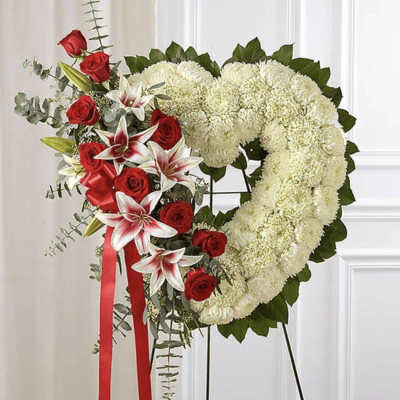 Heart-shaped floral wreath with red roses and white lilies on a stand