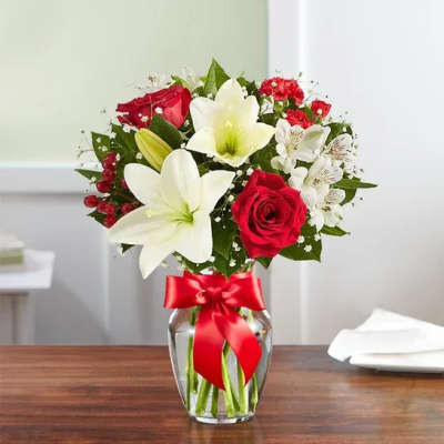 Arrangement of red roses and white lilies in a clear glass vase with a red ribbon bow