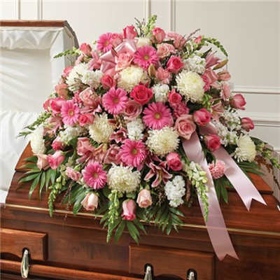 Pink and white floral casket spray with ribbon on a wooden casket