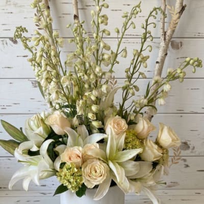 White lilies and cream roses in a white pot with tall birch branches.