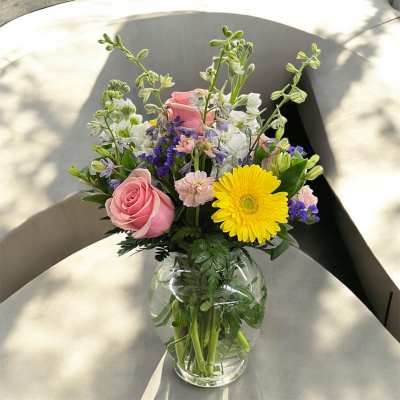 Mixed bouquet of pink roses, yellow gerbera daisy, and pastel flowers in a clear glass vase