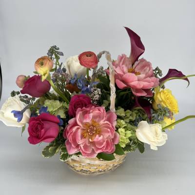 Mixed bouquet in a woven basket with pink, white, yellow, and purple blooms