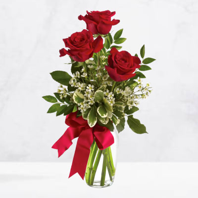 Three red roses in a clear glass vase with a red ribbon