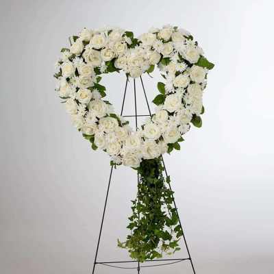 White rose heart wreath on a black easel with trailing greenery