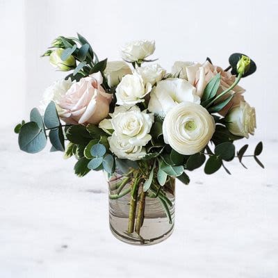 Compact arrangement of white and blush roses and ranunculus with eucalyptus in a clear glass vase