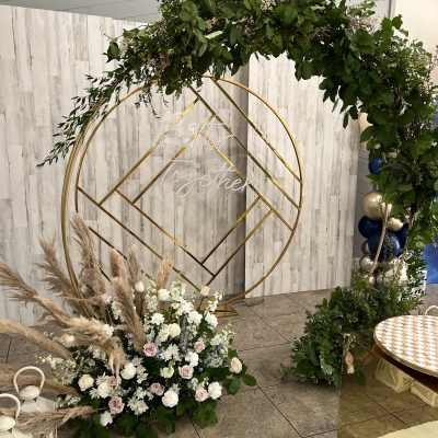 Floral arch with white and blush flowers and greenery beside a gold geometric frame