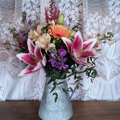 Pink lilies and mixed flowers arranged in a metal pitcher vase