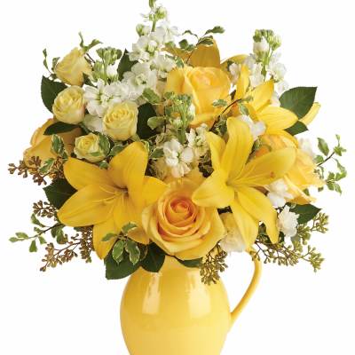 Yellow roses and lilies arranged in a yellow pitcher vase