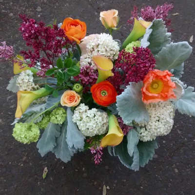 Low arrangement of orange ranunculus and poppies with yellow calla lilies and white hydrangea clusters