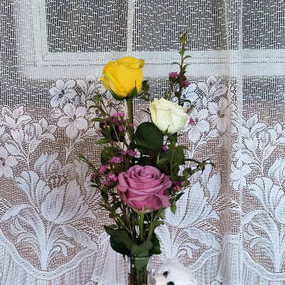 Mixed roses in a glass vase with a small white teddy bear