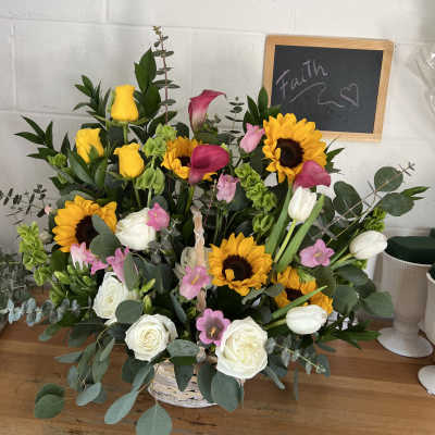 Basket arrangement of yellow roses, sunflowers, white tulips, and pink calla lilies