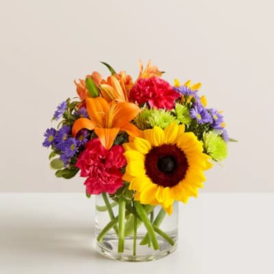 Colorful mixed bouquet in a clear glass vase with a sunflower and lilies