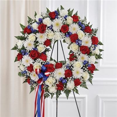 Circular red, white, and blue floral wreath on a stand with ribbon