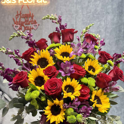 Bouquet of red roses, sunflowers, and purple flowers in a glass vase
