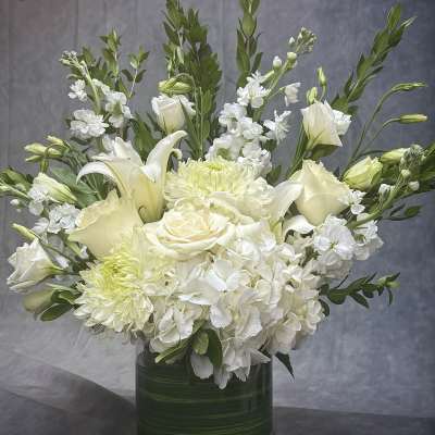 White floral arrangement in a green glass vase with lilies, roses, and hydrangeas
