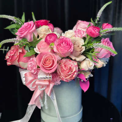 Pink and white roses arranged in a round hatbox with ribbon and pearl accents