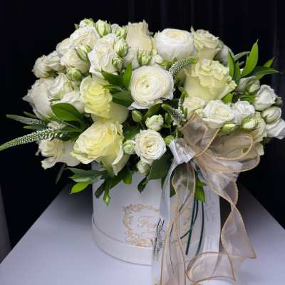 White rose and ranunculus arrangement in a round hatbox with ribbon