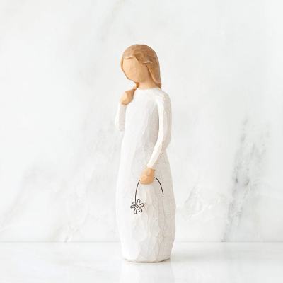 Wooden angel figurine in a white dress holding a small flower