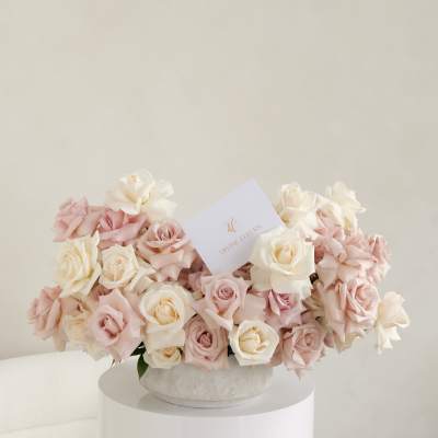 Blush and ivory roses arranged in a round hatbox with a card.