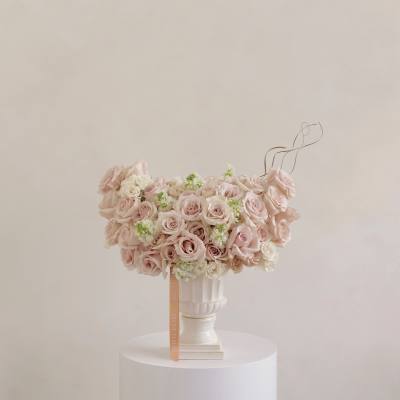 Blush roses and white flowers arranged in a white pedestal vase