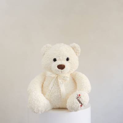 White teddy bear with a ribbon sitting on a pedestal