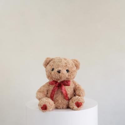 Plush teddy bear with a red heart ribbon sitting on a white pedestal