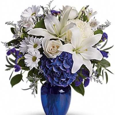 White lilies and daisies arranged with blue flowers in a cobalt vase