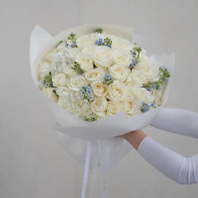 Bouquet of white roses and pale blue accents wrapped in white paper