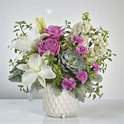 Pink roses and white lilies in a white vase with a succulent accent