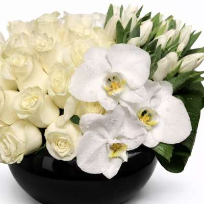 White roses and orchids arranged in a black bowl vase